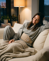 Woman relaxing on a couch wearing the cordless heated cramp relief belt